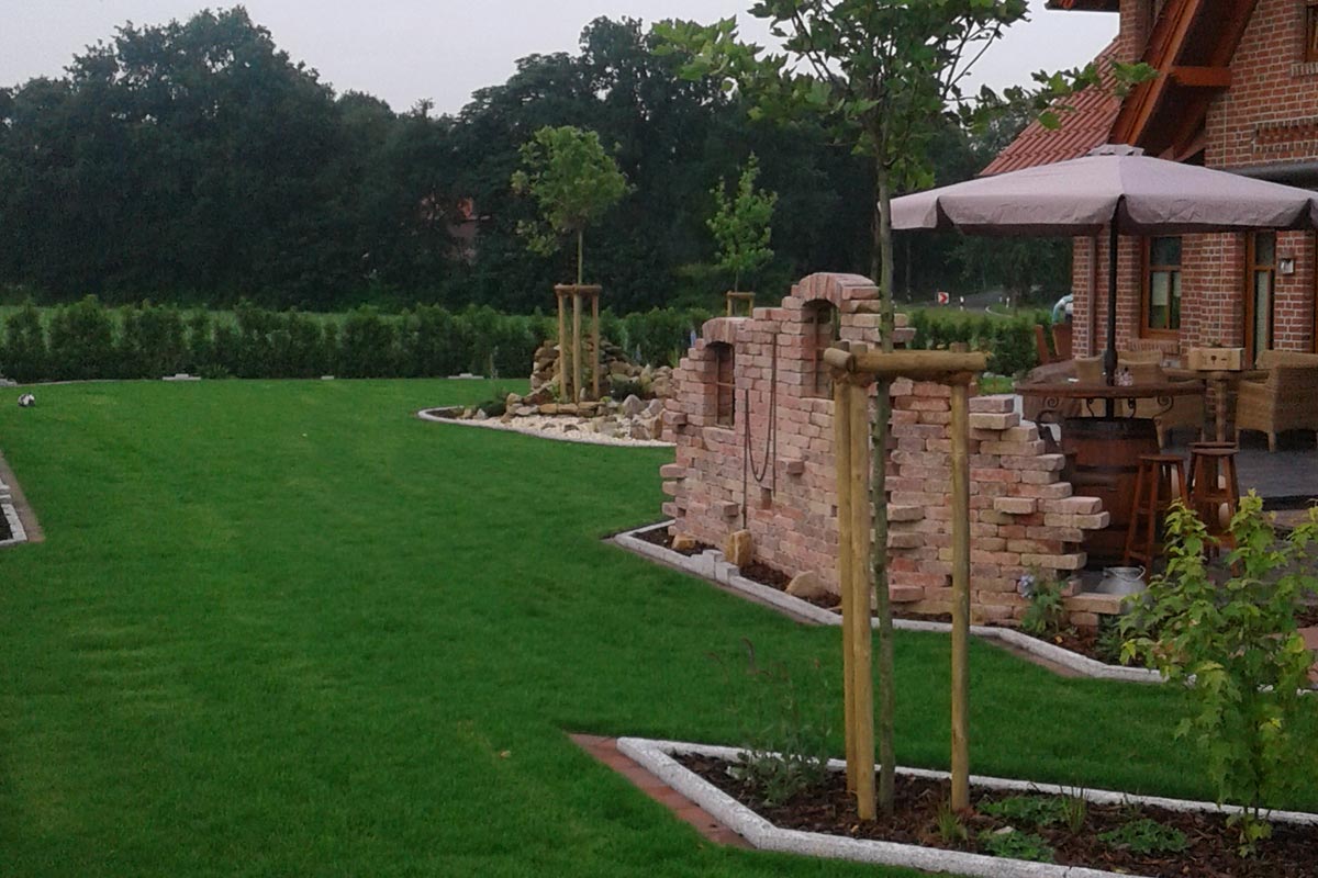 Ein neu gestalteter Garten mit Rasen, Bäumen und einer Ziermauer